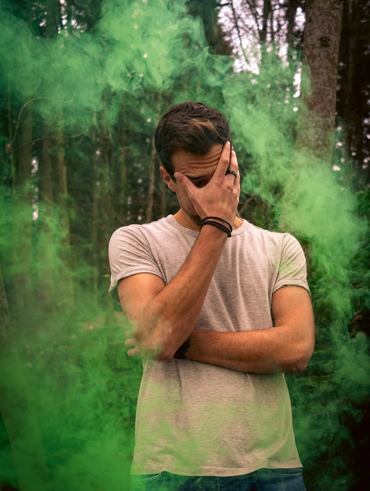 Gabriel Sommer standing in a forest in green smoke, one hand over his face
